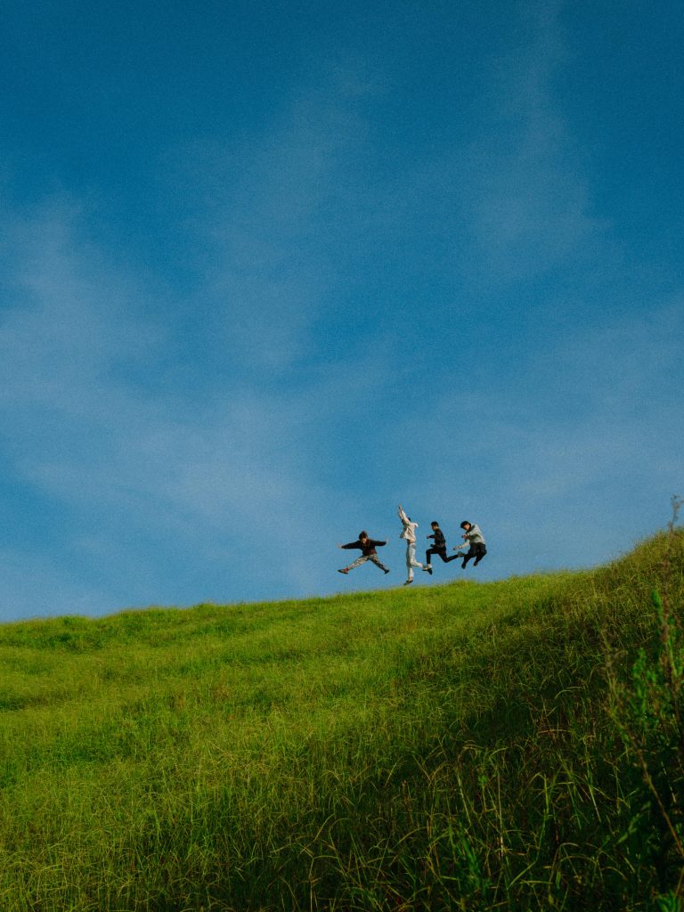 Vibrant scene of friends joyfully jumping on a lush green hill under a clear blue sky.