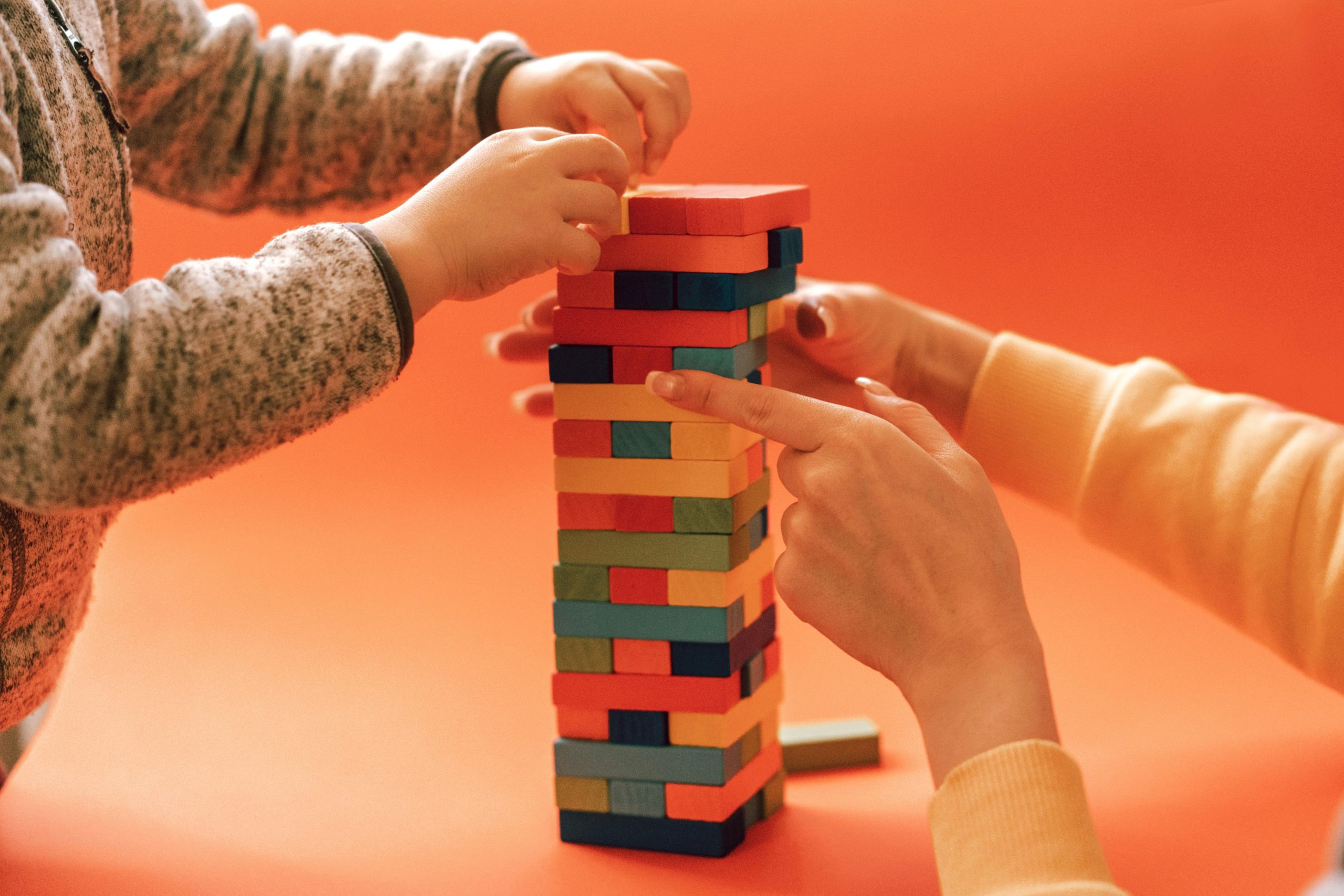 A child and adult play with colorful wooden blocks against an orange backdrop, emphasizing learning and creativity.